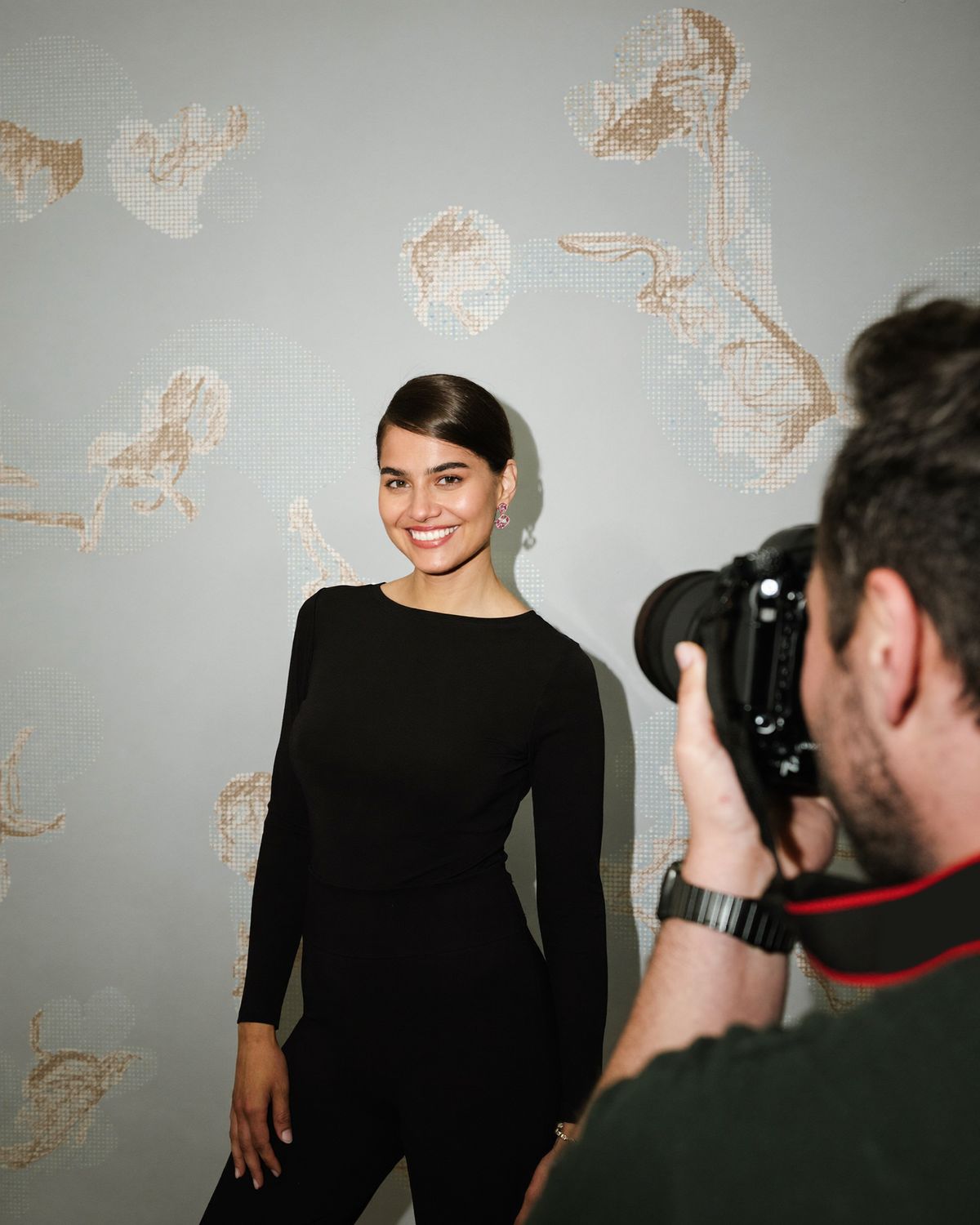 Eine Frau steht vor einer Fotowand, im Vordergrund fotografiert sie ein Fotograf